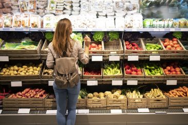 Good looking woman standing in front of vegetable shelves choosing what to buy.